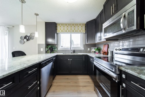 U-shaped kitchen featuring dark wood cabinetry, light-toned granite countertops, stainless steel appliances, and a subway tile backsplash - 117 2229 44 Avenue, Edmonton, AB - Indoor Photo Showing Kitchen With Upgraded Kitchen