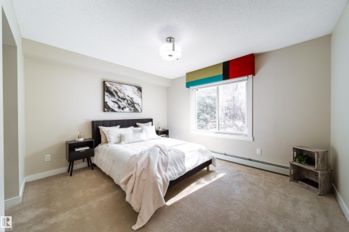 Light-filled room featuring a large window, neutral wall tones, textured carpet flooring, baseboard heating, and an overhead flush-mount light fixture - 117 2229 44 Avenue, Edmonton, AB - Indoor Photo Showing Bedroom