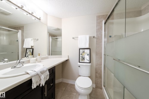 Full bathroom featuring a dark wood-finish vanity with an integrated sink, a large wall-mounted mirror, and a shower with frosted glass doors - 117 2229 44 Avenue, Edmonton, AB - Indoor Photo Showing Bathroom