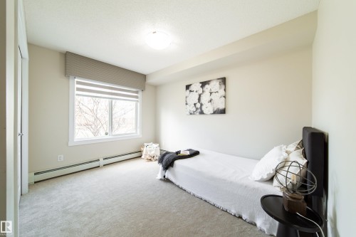 Carpeted room featuring a large window with horizontal blinds, overhead flush-mount lighting, and baseboard heating - 117 2229 44 Avenue, Edmonton, AB - Indoor