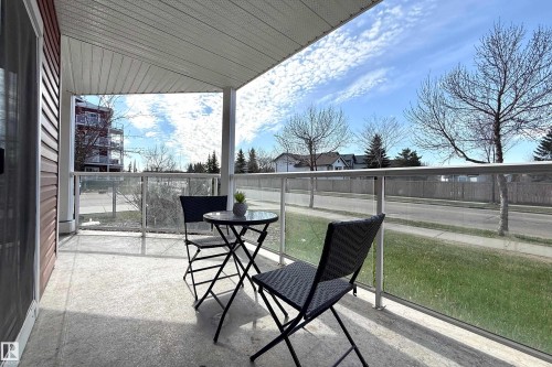 Covered outdoor patio with a concrete floor, white soffit ceiling, and glass panel railings - 117 2229 44 Avenue, Edmonton, AB - Outdoor