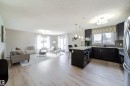 Open-concept living area featuring light wood-finish flooring, a kitchen island with pendant lighting, dark cabinetry, stainless steel appliances, and multiple windows - 117 2229 44 Avenue, Edmonton, AB  - Indoor 