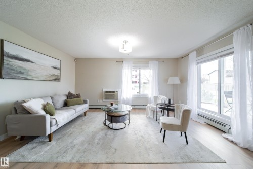 Bright living area featuring wood-finish flooring, light-colored walls, and a large window with a sliding glass door - 117 2229 44 Avenue, Edmonton, AB - Indoor Photo Showing Living Room