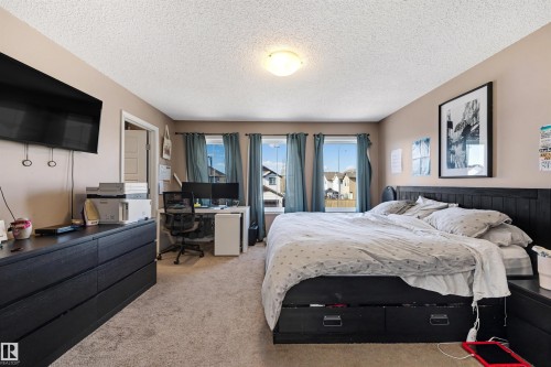 Carpeted room featuring a built-in ceiling light fixture, neutral wall tones, and three windows with curtains - 6115 18 Avenue, Edmonton, AB - Indoor Photo Showing Bedroom