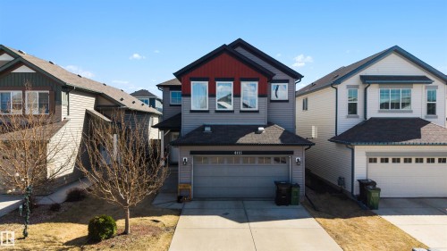 Contemporary two-story residence featuring a two-car garage with overhead door, a concrete driveway, and siding exterior with red and dark gray accents - 6115 18 Avenue, Edmonton, AB - Outdoor With Facade
