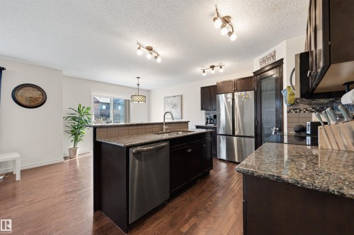 Kitchen featuring dark wood-finish cabinetry, granite countertops, stainless steel appliances, a tiled backsplash, and wood-finish flooring - 6115 18 Avenue, Edmonton, AB - Indoor Photo Showing Kitchen