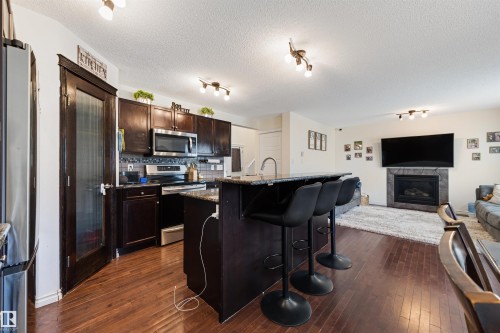 Open-concept kitchen featuring dark wood cabinetry, stainless steel appliances, and a mosaic tile backsplash - 6115 18 Avenue, Edmonton, AB - Indoor Photo Showing Kitchen With Fireplace With Upgraded Kitchen