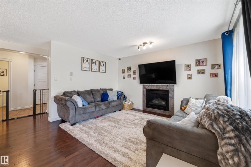 Living area featuring wood-finish flooring, white walls, and a tiled fireplace surround - 6115 18 Avenue, Edmonton, AB - Indoor Photo Showing Living Room With Fireplace