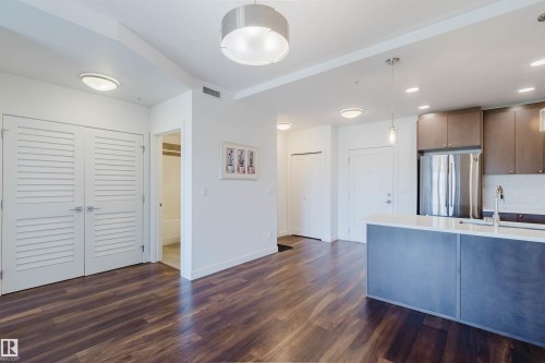 Open-concept living area with wood-finish flooring, recessed lighting, and a modern kitchen island with an integrated sink - 205 1316 Windermere Way, Edmonton, AB - Indoor Photo Showing Kitchen