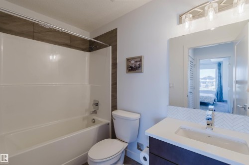 Bathroom featuring a white bathtub and shower combination with a brown-toned tile surround - 205 1316 Windermere Way, Edmonton, AB - Indoor Photo Showing Bathroom