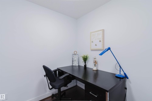 Compact room featuring white walls, dark wood-finish flooring, and a built-in corner desk with dark cabinetry and silver hardware - 205 1316 Windermere Way, Edmonton, AB - Indoor Photo Showing Office