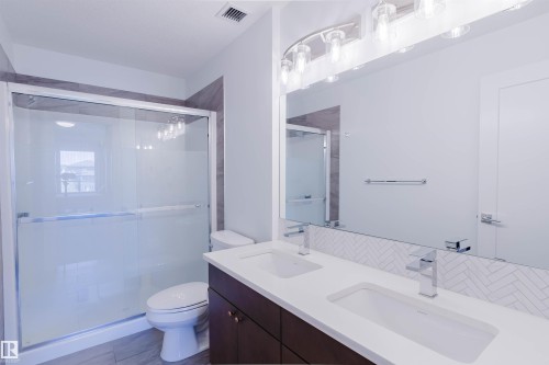 Double vanity with integrated rectangular sinks, chrome faucets, and a herringbone tile backsplash - 205 1316 Windermere Way, Edmonton, AB - Indoor Photo Showing Bathroom