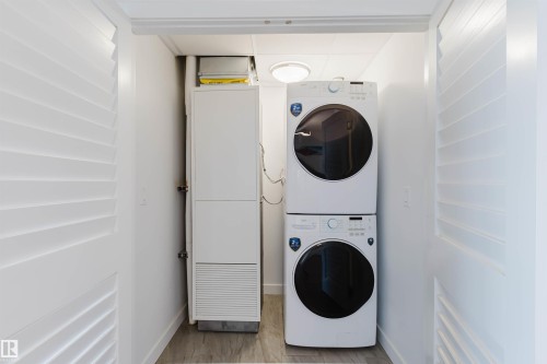 Dedicated laundry closet featuring a stacked washer and dryer set, louvered bi-fold doors, wood-finish flooring, and a ceiling-mounted light fixture - 205 1316 Windermere Way, Edmonton, AB - Indoor Photo Showing Laundry Room