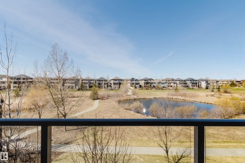 Balcony with glass railing overlooking a pond, walking path, and a residential community - 205 1316 Windermere Way, Edmonton, AB - Outdoor With Balcony With View