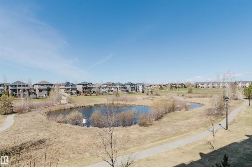 Pond-front property featuring a walking path, surrounding green space, and residential architecture - 205 1316 Windermere Way, Edmonton, AB - Outdoor With View