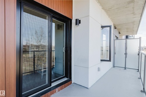Private balcony featuring a sliding glass door, contemporary wall sconce, frosted glass panels, and a concrete ceiling - 205 1316 Windermere Way, Edmonton, AB - Outdoor With Balcony With Exterior