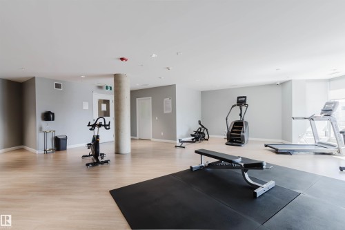 Spacious fitness area featuring wood-finish flooring, light gray walls, and large windows - 205 1316 Windermere Way, Edmonton, AB - Indoor Photo Showing Gym Room