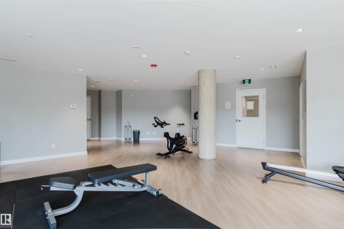 Spacious fitness area featuring wood-finish flooring, light gray walls, a central structural column, and recessed ceiling lighting - 205 1316 Windermere Way, Edmonton, AB - Indoor Photo Showing Gym Room