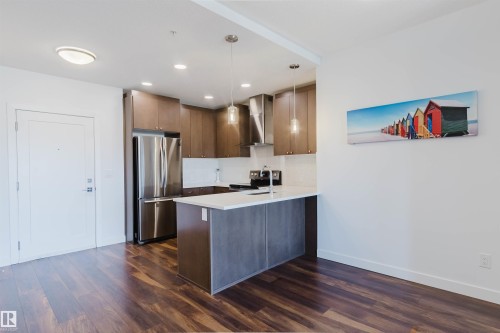 Open-concept kitchen featuring wood-finish flooring, stainless steel appliances, a kitchen island with seating, pendant lighting, and recessed ceiling lights - 205 1316 Windermere Way, Edmonton, AB - Indoor Photo Showing Kitchen With Stainless Steel Kitchen