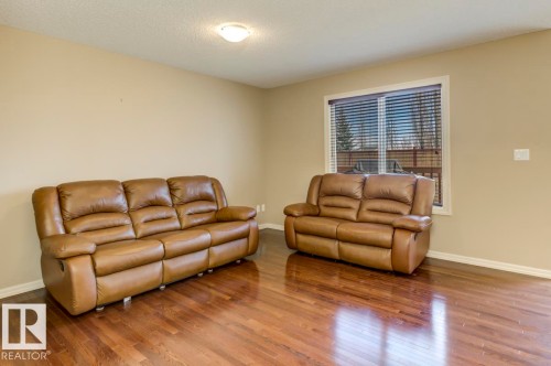 Spacious room featuring wood-finish flooring, neutral-toned walls, and white trim - 119 Rue Monique, Beaumont, AB - Indoor Photo Showing Living Room