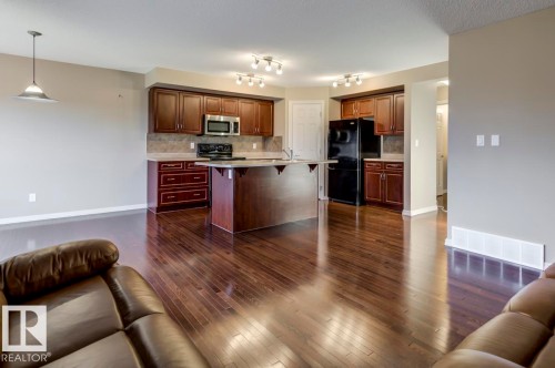 Kitchen featuring dark wood cabinetry, a central island with a breakfast bar, stainless steel microwave, and black refrigerator and range - 119 Rue Monique, Beaumont, AB - Indoor Photo Showing Kitchen