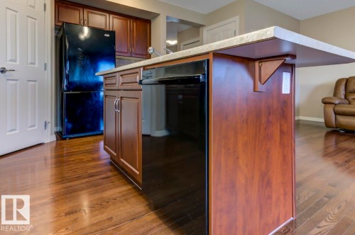 Kitchen island with a light-toned countertop, integrated dishwasher, and dark wood-finish cabinetry - 119 Rue Monique, Beaumont, AB - Indoor