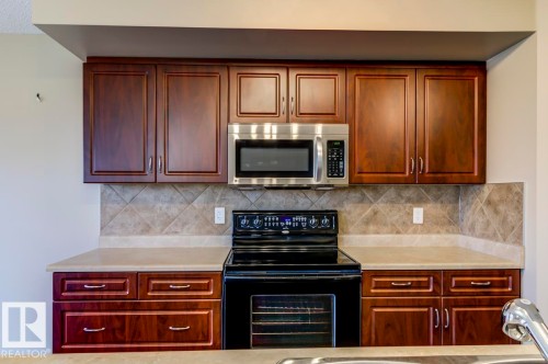 Kitchen featuring rich wood-finish cabinetry, a stainless steel over-the-range microwave, and a black electric range - 119 Rue Monique, Beaumont, AB - Indoor Photo Showing Kitchen