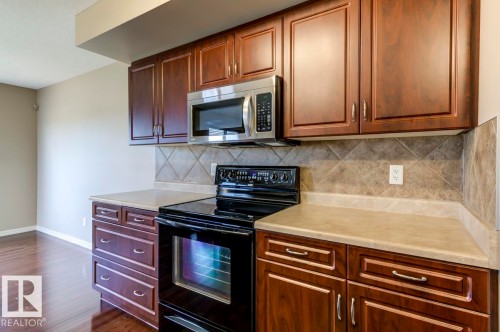 Kitchen featuring wood-finish cabinetry, light-toned countertops, a tile backsplash with diamond accents, a black electric range, and a stainless steel microwave - 119 Rue Monique, Beaumont, AB - Indoor Photo Showing Kitchen