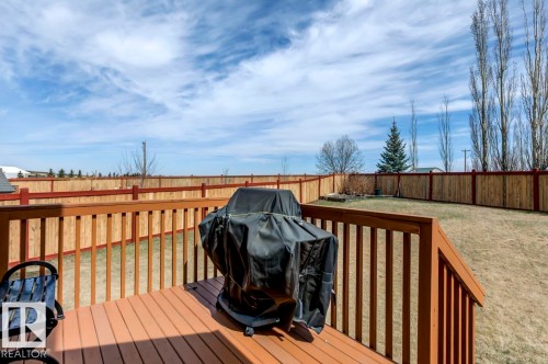 Expansive backyard featuring a wood deck with railings, a perimeter wooden fence, a grassy lawn, and mature trees - 119 Rue Monique, Beaumont, AB - Outdoor With Deck Patio Veranda