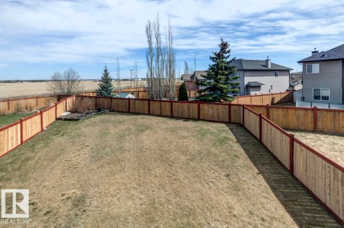 Expansive backyard featuring wood privacy fencing with red-stained posts, a manicured lawn, and an established garden bed - 119 Rue Monique, Beaumont, AB - Outdoor