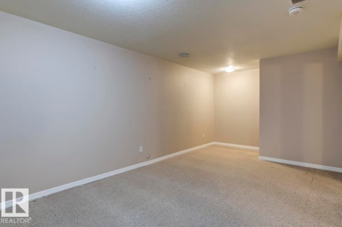 Spacious room featuring neutral carpeting, light-toned wall paint, and white baseboards - 119 Rue Monique, Beaumont, AB - Indoor Photo Showing Other Room