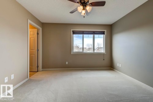 Carpeted room featuring a ceiling fan with integrated lighting, a large window with blinds, and a paneled interior door - 119 Rue Monique, Beaumont, AB - Indoor Photo Showing Other Room