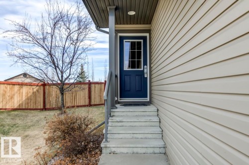 Light beige horizontal siding exterior with a contrasting navy blue entry door featuring clear glass panes - 119 Rue Monique, Beaumont, AB - Outdoor