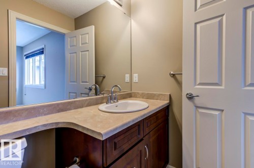Bathroom vanity featuring a light-toned countertop, undermount sink, chrome faucet, and dark wood-finish cabinetry - 119 Rue Monique, Beaumont, AB - Indoor Photo Showing Bathroom