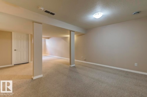 Spacious room featuring neutral carpet flooring, light beige painted walls, white trim, and a surface-mounted ceiling light fixture - 119 Rue Monique, Beaumont, AB - Indoor Photo Showing Other Room
