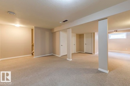Expansive carpeted area featuring light neutral wall colors, flush-mounted lighting, multiple white panel doors, and a natural wood-finish staircase - 119 Rue Monique, Beaumont, AB - Indoor