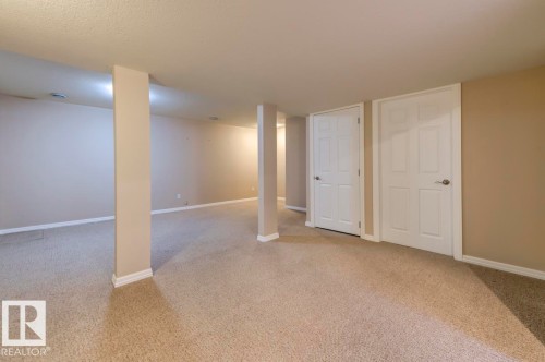 Expansive carpeted area featuring light beige walls, white baseboards, recessed lighting, and white paneled doors with silver hardware - 119 Rue Monique, Beaumont, AB - Indoor Photo Showing Other Room