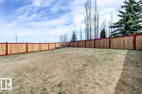 Expansive backyard featuring a full perimeter wood fence with red-stained posts and top rails - 119 Rue Monique, Beaumont, AB - Outdoor