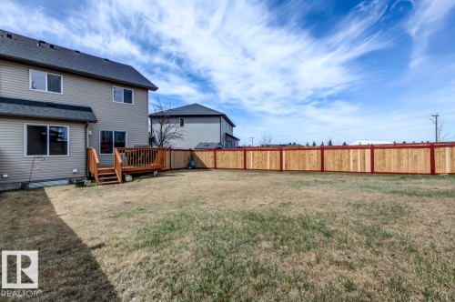 Spacious backyard featuring an expansive lawn, a newly installed wood privacy fence with contrasting posts, and a wood-finish deck with stairs leading to the yard - 119 Rue Monique, Beaumont, AB - Outdoor
