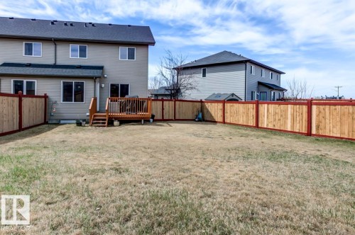 Spacious rear yard featuring a wooden privacy fence with red trim, a multi-level wooden deck, and a light-colored vinyl siding exterior - 119 Rue Monique, Beaumont, AB - Outdoor