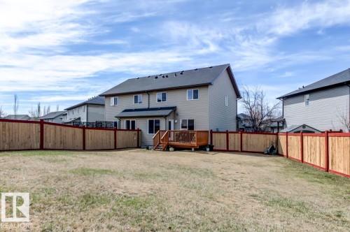 Rear exterior featuring a wood deck with stairs, beige siding, white trim windows, and a dark shingle roof - 119 Rue Monique, Beaumont, AB - Outdoor
