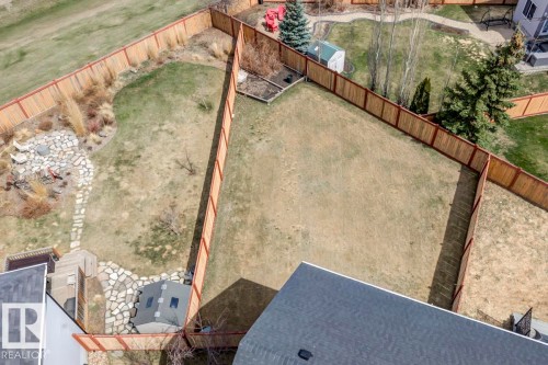 Expansive fenced backyard featuring a large grass area, a dedicated rock landscaping section, and a stone pathway - 119 Rue Monique, Beaumont, AB - Outdoor