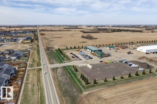Aerial perspective featuring a commercial property with multiple buildings, extensive paved parking, and a large unpaved lot - 119 Rue Monique, Beaumont, AB - Outdoor With View