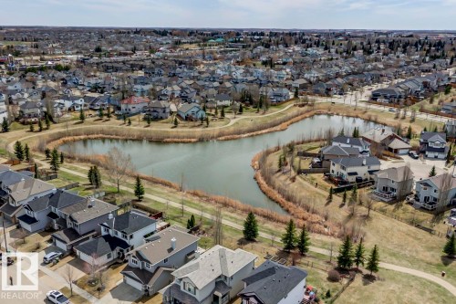 Aerial perspective showcasing a residential community with a central pond - 119 Rue Monique, Beaumont, AB - Outdoor With View