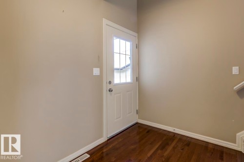 Entryway featuring a white door with divided lites, dark wood-finish flooring, and light-toned walls - 119 Rue Monique, Beaumont, AB - Indoor Photo Showing Other Room
