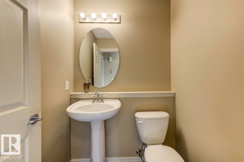 Pedestal sink with a polished chrome faucet, an oval mirror, and a four-bulb vanity light fixture - 119 Rue Monique, Beaumont, AB - Indoor Photo Showing Bathroom