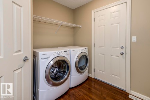 Dedicated laundry space featuring a wire shelf, warm beige wall tones, and wood-finish flooring - 119 Rue Monique, Beaumont, AB - Indoor Photo Showing Laundry Room