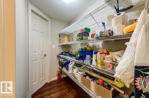 Utility room with dark wood-finish flooring, white wire shelving, light-toned walls, and a white paneled door - 119 Rue Monique, Beaumont, AB - Indoor Photo Showing Other Room