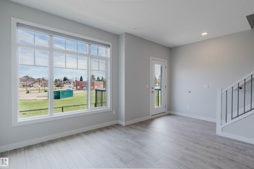 Spacious room featuring a large multi-pane window, wood-finish flooring, recessed ceiling lighting, a glass-panel exterior door, and a staircase with an open-rail design - 3 11373 12 Avenue, Edmonton, AB - Indoor Photo Showing Other Room