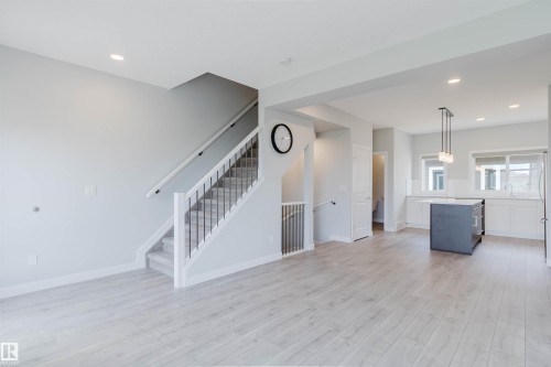 Open-concept living space featuring light wood-finish flooring, a contemporary staircase with black metal balusters, recessed lighting, a modern kitchen island with pendant lighting, and white cabinetry - 3 11373 12 Avenue, Edmonton, AB - Indoor